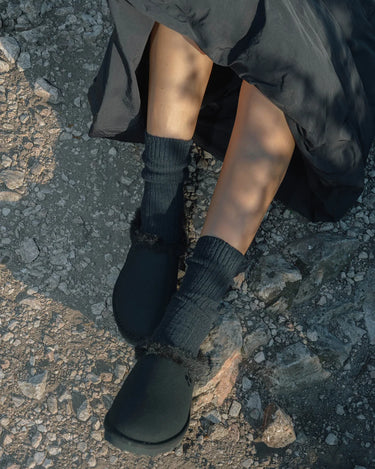 Person wearing black slippeers and black skirt on a textured pavement