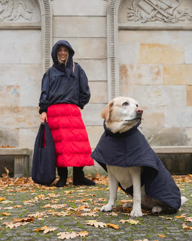 Woman and dog wearing matching black coats in an urban setting with stone architecture.