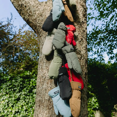 Brown winter gloves made from vegan recycled materials hanging on tree branches. - The New Orchard CH