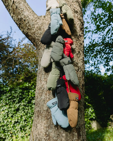 Brown winter gloves made from vegan recycled materials hanging on tree branches. - The New Orchard CH
