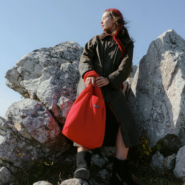 Person holding a red bag on rocky terrain with a clear blue sky