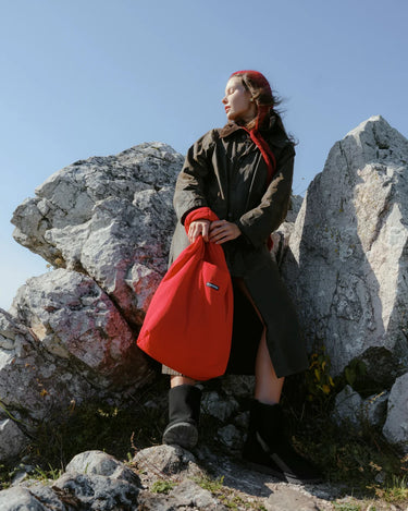 Person holding a red bag on rocky terrain with a clear blue sky