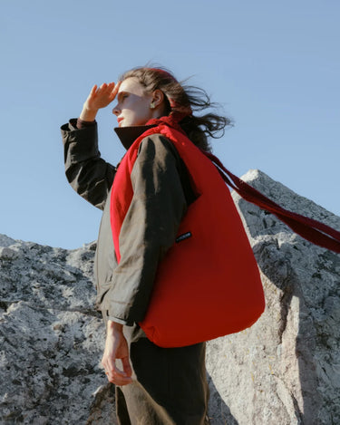 Person with a red bag standing on rocky terrain against a clear blue sky