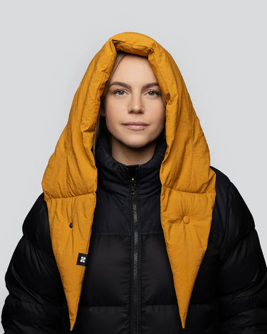 Amber yellow vegan winter capuche made from recycled materials worn over black puffer jacket. - The New Orchard CH