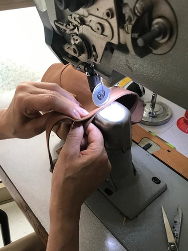 Person working with vegan leather on a sewing machine in a workshop setting.
