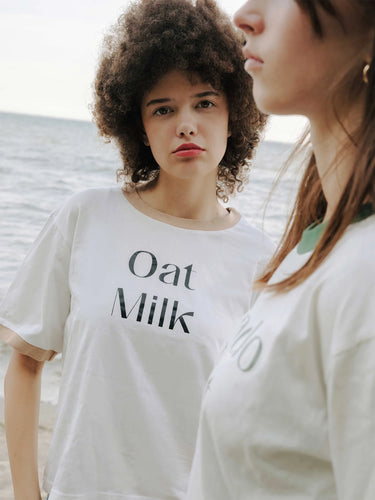 Two women wearing white t-shirts with 'Oat Milk' text, standing close together.