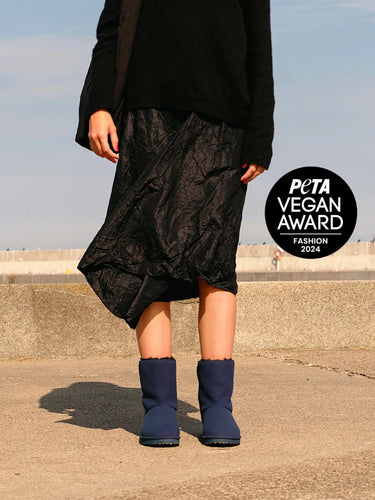 Person wearing a black outfit with navy boots on a concrete surface, PETA Vegan Award logo visible.