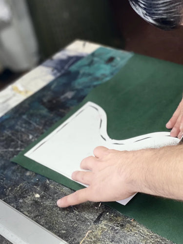 Person cutting a green sheet of material with scissors useing white tailoring template