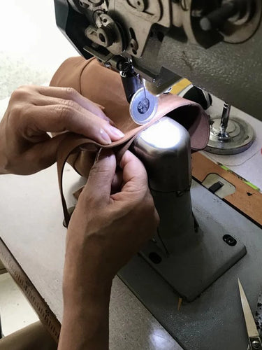 Person sewing vegan leather on a sewing machine with a close-up view of hands and equipment.