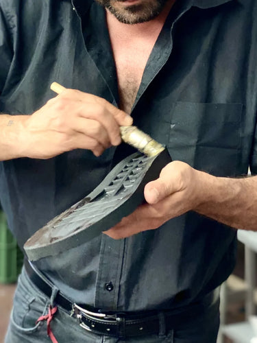 Man working on a shoe sole with a tool, wearing a black shirt.