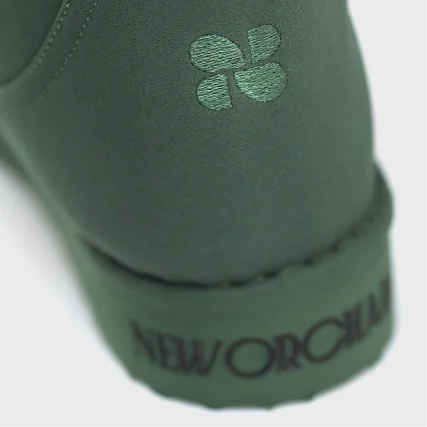 Close-up of a green shoe with a logo and 'New Orchard' text on a white background
