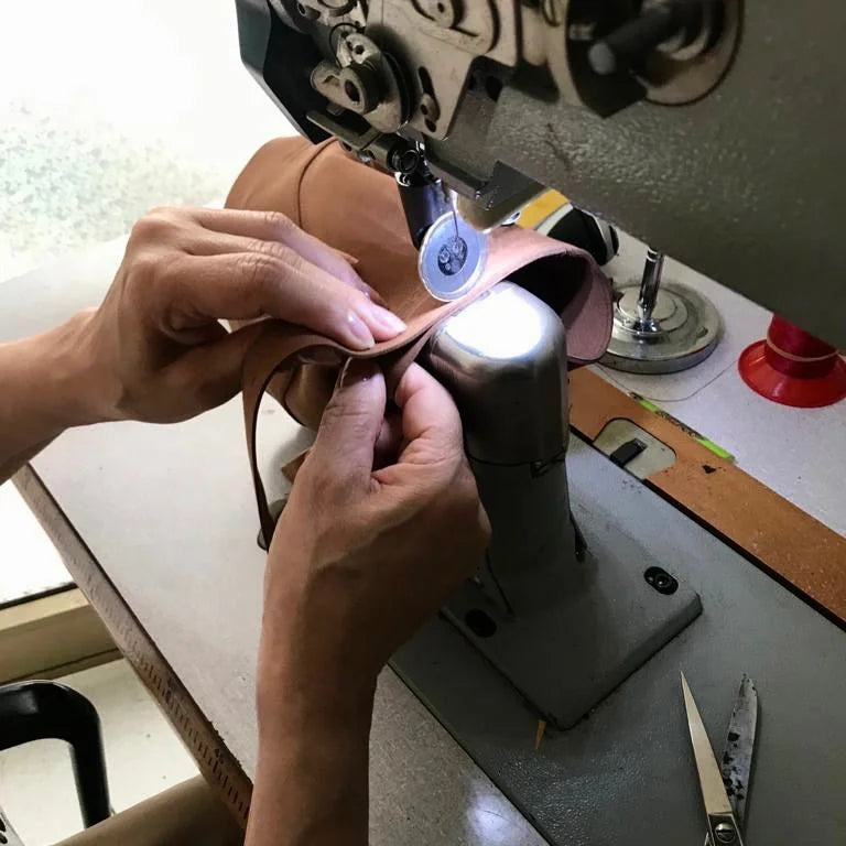 Person using a sewing machine to work on a brown vegan leather item.